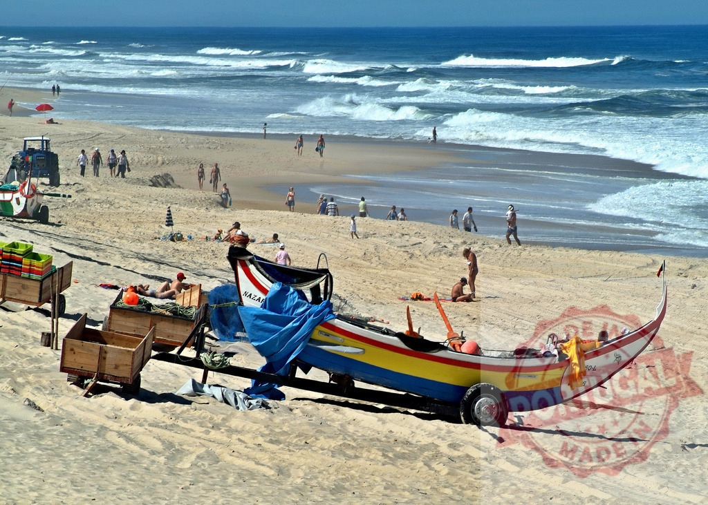 Traditional fishing boats on Nazaré beach in Portugal | Colorful fishing boats resting on the sand while people enjoy the sun and ocean waves - Realisiert mit Pictrs.com