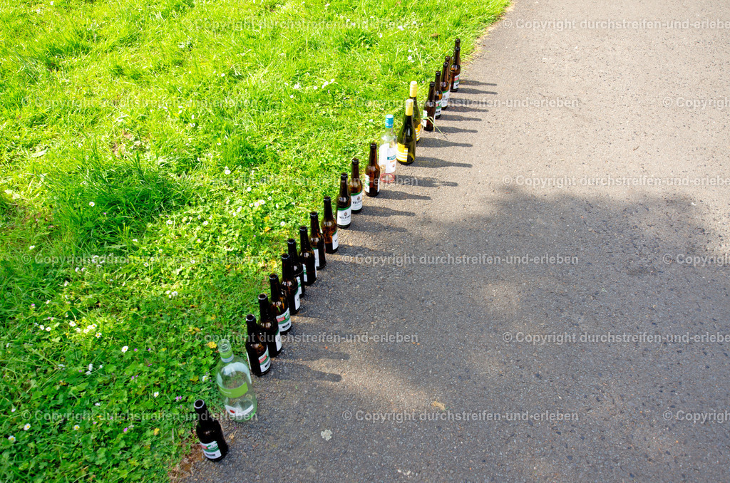 Bier- und Weinfreuden am Vatertag | Im Grünen haben Feiernde an Christi Himmelfahr Bier- und Weinflaschen zu einer menschlich wirkenden Schlange aufgestellt. - Realisiert mit Pictrs.com