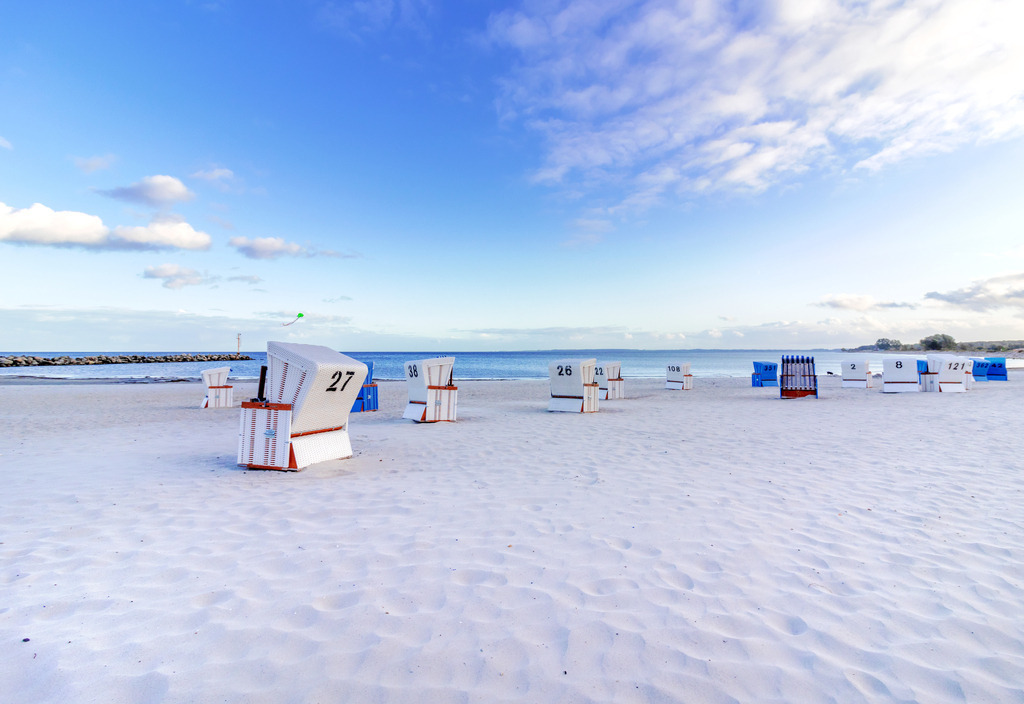 Wandbild: Abendliche Lichtstimmung am Strand in Damp | Ein traumhafter Abend am Strand von Damp – die sanfte Lichtstimmung taucht die Küstenlandschaft in eine magische Atmosphäre. Zahlreiche Strandkörbe stehen auf dem feinen Sand, bereit für einen entspannten Ausblick auf das Meer. Der Himmel leuchtet in sanften Blautönen mit einigen Wolken, die die friedliche Stimmung unterstreichen. Dieses Wandbild bringt maritimes Flair und die beruhigende Schönheit der Ostseeküste direkt in Ihr Zuhause. - Realisiert mit Pictrs.com