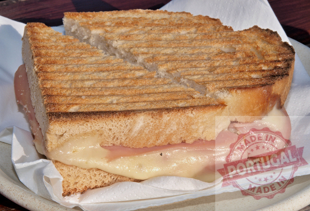 Grilled cheese ham panini sandwich served on a plate | Grilled ham and cheese panini cut in half, showcasing layers of melted cheese - Realized with Pictrs.com