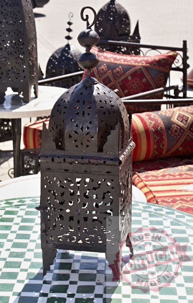 Moroccan metal lantern on tiled table in souk | Ornate metal lantern sitting on a green and white tiled table with patterned cushions in the background - Realized with Pictrs.com