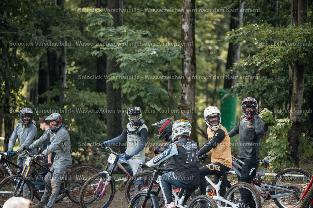 Mountainbiker vor dem Start | Die Aufnahme zeigt eine Gruppe von Mountainbikern in voller Montur, die sich in einem dichten Wald versammelt haben. Die Biker tragen Helme, Schutzbrillen und spezielle Mountainbike-Bekleidung. Ihre Fahrräder stehen in der Nähe, bereit für den Start. Die Szene vermittelt eine Atmosphäre der Vorfreude und Konzentration vor einem Wettkampf. - Realisiert mit Pictrs.com