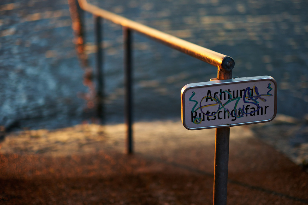Geländer mit Vorsicht Rutschgefahr Hinweis | Bregenz, Austria - June 07, 2024: Geländer mit Vorsicht Rutschgefahr Hinweis im Abendlicht. - Realisiert mit Pictrs.com