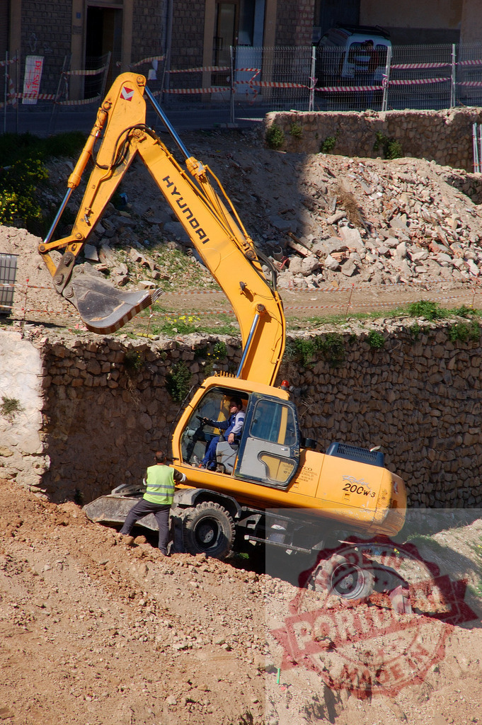 Hyundai excavator working on construction site digging dirt | Hyundai excavator digging fresh dirt with workers on a new commercial construction site - Realized with Pictrs.com