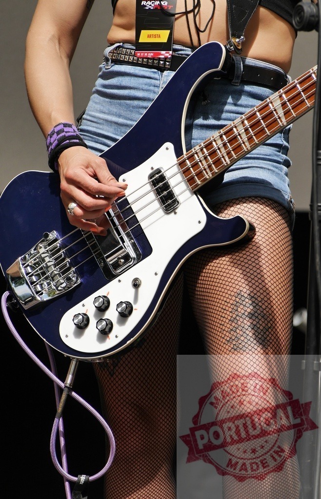 Woman playing bass guitar during live concert performance | Woman playing a Rickenbacker bass guitar with fishnet stockings and a tattoo at a music festival - Realisiert mit Pictrs.com
