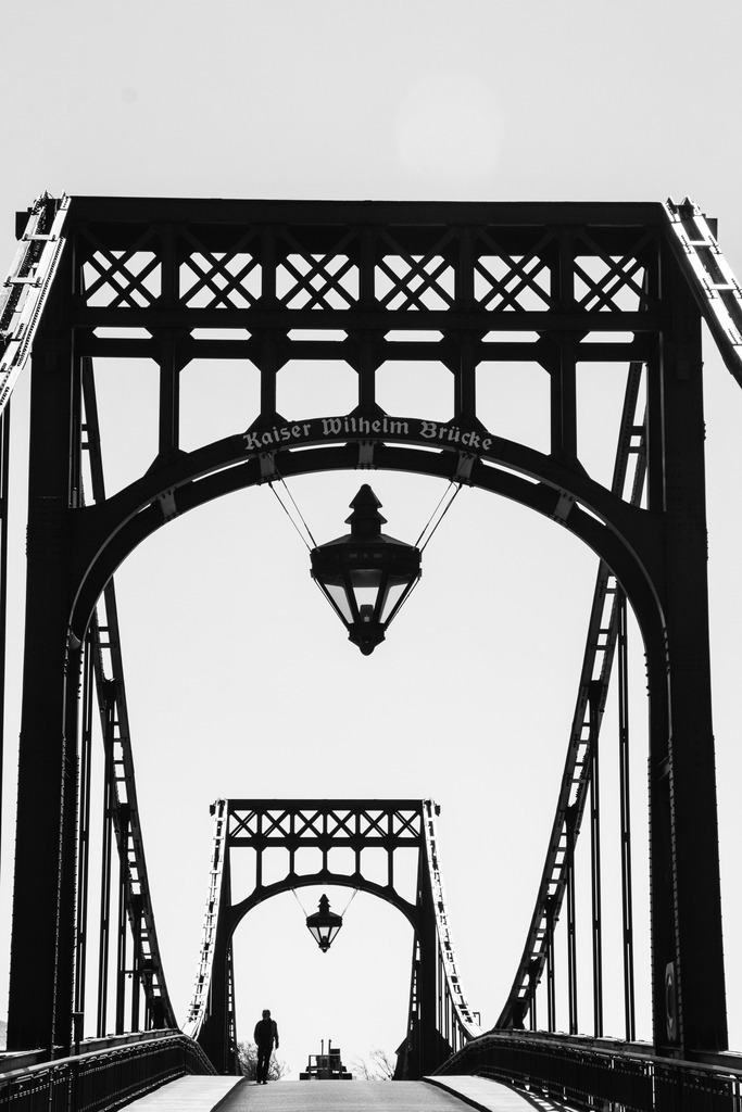 Schwarz-Weiß-Brücke zwischen Einsamkeit und Hoffnung | Brücke als kraftvolle Schwarz-Weiß-Komposition: ein Mensch auf dem Weg, eingerahmt von stählerner Strenge und stiller Weite. - Realisiert mit Pictrs.com