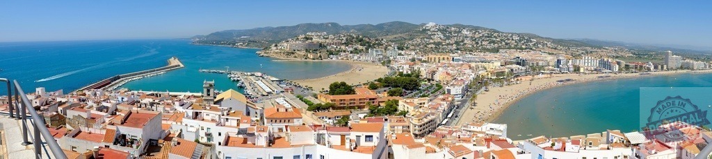 Panoramic view of Peniscola showcasing the beach, port, and cityscape under a clear blue sky | Aerial cityscape of Peniscola, Spain, highlighting the beach, port, and urban area on a sunny day - Realisiert mit Pictrs.com