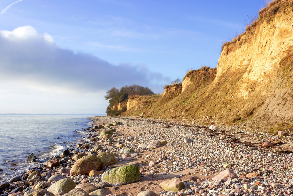 Wandbild: Steilküste in Kleinwaabs im Winter | Dieses Wandbild im Querformat zeigt die markante Steilküste von Waabs mit sandig-tonigen Klippen, die sich steil aus dem felsigen Ufer erheben. Im Vordergrund liegen Steine und Kiesel, während die sanften Wellen der Ostsee gegen das Ufer schlagen. Das Sonnenlicht bringt die Struktur und Farbigkeit der Klippen zur Geltung, während der Himmel mit leichten Wolken die Szene abrundet. Ein kraftvolles Küstenmotiv, das die geologische Vielfalt und die stille Energie der Ostsee einfängt – ideal für Wohnräume, Ferienunterkünfte oder Praxisräume mit maritimem Bezug. Erhältlich als Leinwand, Acrylglas, Alu-Dibond, hochwertiger FineArt-Druck oder als schallabsorbierendes Akustikbild. - Realisiert mit Pictrs.com