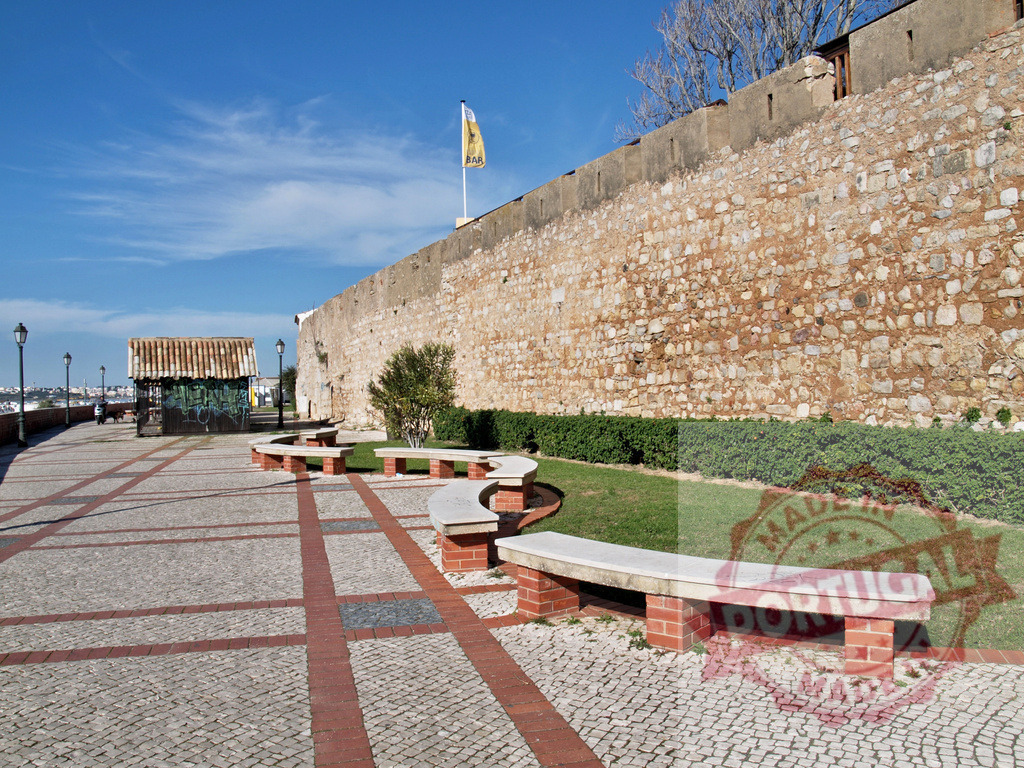 Lagos city wall promenade with stone benches | Historic city wall and stone benches along a promenade under a blue sky in Lagos, Portugal - Realized with Pictrs.com