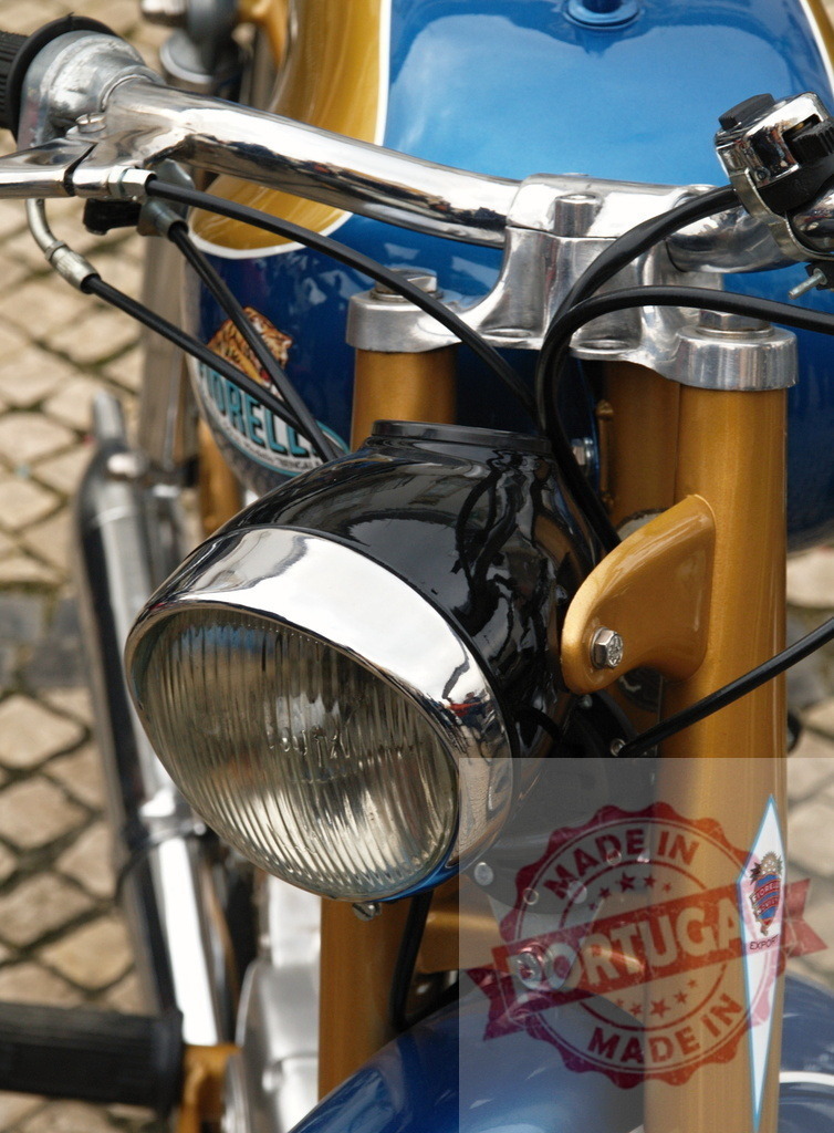 Close-up of Headlight and Handlebars of a Vintage Moto Morini Motorcycle | Shiny chrome headlight and handlebars of a blue and gold vintage Moto Morini motorcycle, showcasing its classic design - Realized with Pictrs.com