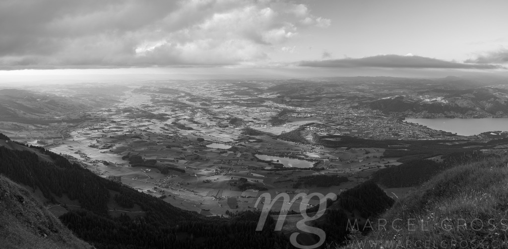 Simmental Valley Panorama, Bernese Alps, Switzerland | A sweeping panoramic view showcases the lush Simmental valley in Switzerland, bathed in soft sunlight filtering through scattered clouds. The valley floor is a patchwork of green meadows and small villages, with a lake visible in the distance, creating a tranquil and picturesque scene. - Realisiert mit Pictrs.com