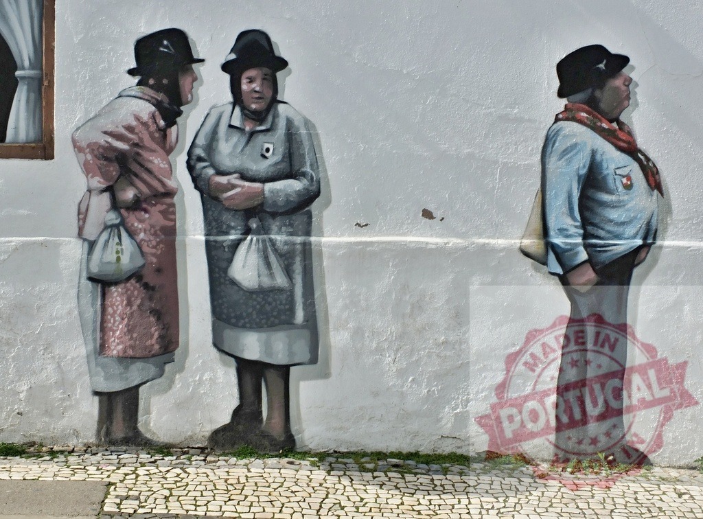 Street art mural depicting older people wearing traditional clothing | Street art mural depicting three older people in traditional clothing on a white wall above cobblestones - Realisiert mit Pictrs.com