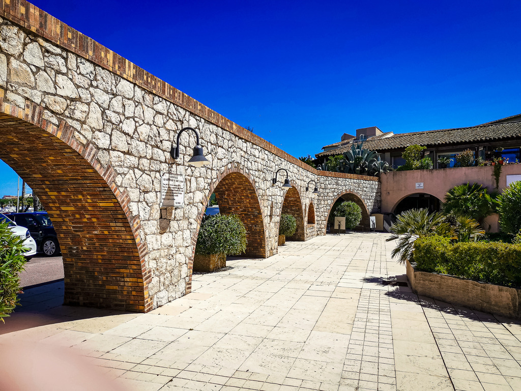 Wandbild Kunstdruck Poster – Antibes Steinbogen: Mediterrane Architektur im Sommerlicht von Robert Steinke | Hol dir den exklusiven Glanz und die zeitlose Eleganz der französischen Riviera direkt in deine Wohnräume. Diese beeindruckende Architekturfotografie aus Antibes fängt einen magischen Moment an der Côte d’Azur ein. Der Blick führt durch eine historische, schattige Steinbogen-Passage direkt hinaus auf das sonnenüberflutete, tiefblaue Mittelmeer. Die warmen Natursteintöne des Bogens und das strahlende Sommerlicht im Hintergrund erzeugen eine faszinierende Tiefe und holen das unbeschwerte mediterrane Lebensgefühl perfekt in jeden Raum.Dieses luxuriöse und harmonische Motiv ist der perfekte architektonische Blickfang für ein modernes Wohnzimmer, das repräsentative Büro, ein helles Design-Loft oder für eine einladende, sonnige Atmosphäre im Flur und Schlafzimmer. Um die extremen Kontraste, das goldene Licht der Steine und die brillante Tiefe des Meeres perfekt zur Geltung zu bringen, empfehle ich den Druck auf unseren Premium-Materialien: Erlebe kinoreife Tiefenwirkung und Leuchtkraft auf edlem Acrylglas, ein hochmodernes, reflexionsfreies Finish auf robustem Alu-Dibond oder klassischen Galerie-Charakter auf einer matten Leinwand. Bring exklusives Urlaubsflair an deine Wand! - Realisiert mit Pictrs.com