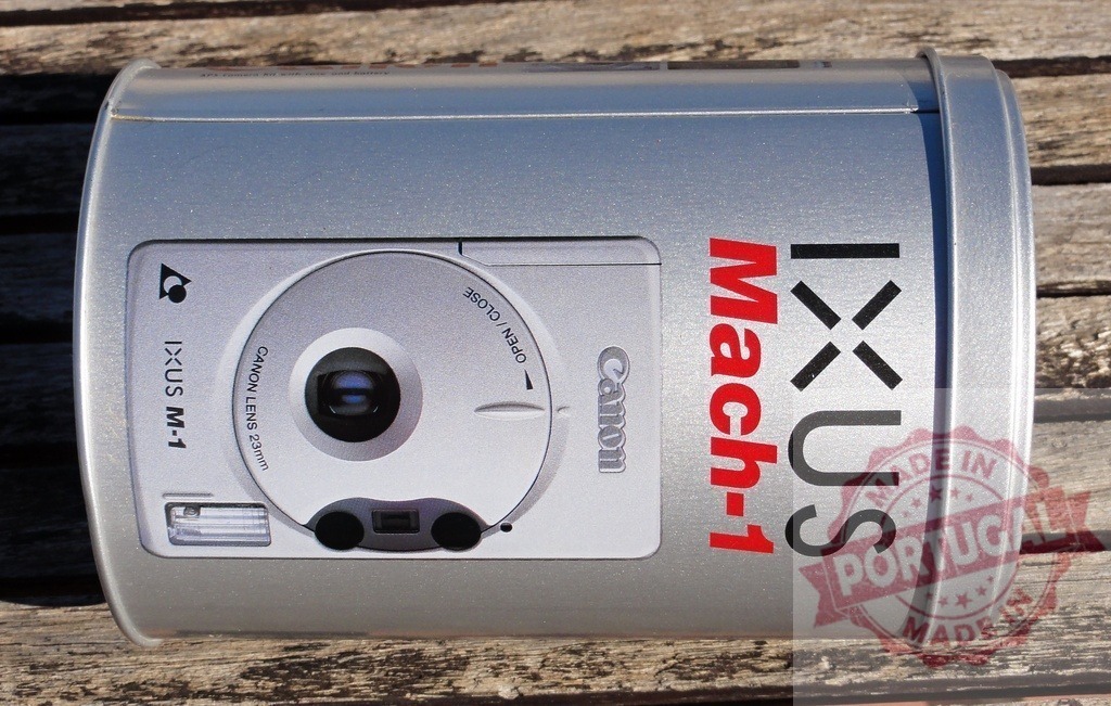 Canon IXUS Mach-1 camera metal tin packaging | Canon IXUS Mach-1 promotional packaging on a wooden background - Realized with Pictrs.com