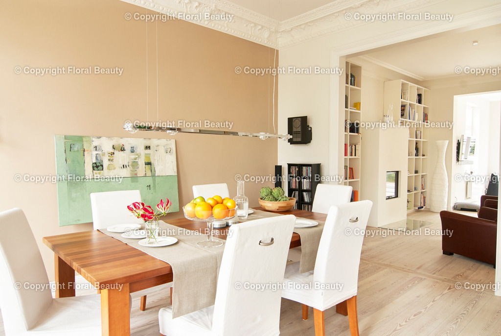 Esszimmer | Esstisch mit weißen Stühlen. Beige Wandfarbe. Schalen mit Artischocken und Obst auf dem Tisch. Blick ins Kaminzimmer. Grünes Wandbild. - Realisiert mit Pictrs.com