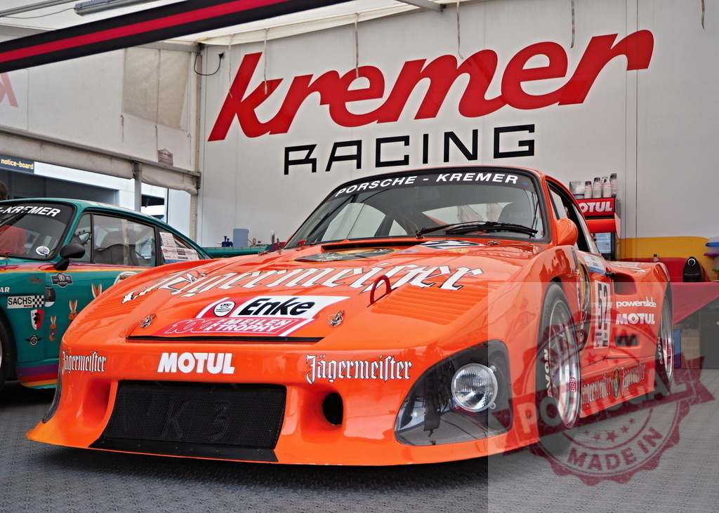 Porsche 935 K3 Jägermeister Kremer Racing car pit | Orange Porsche 935 K3 Jägermeister race car parked inside a Kremer Racing garage - Realized with Pictrs.com