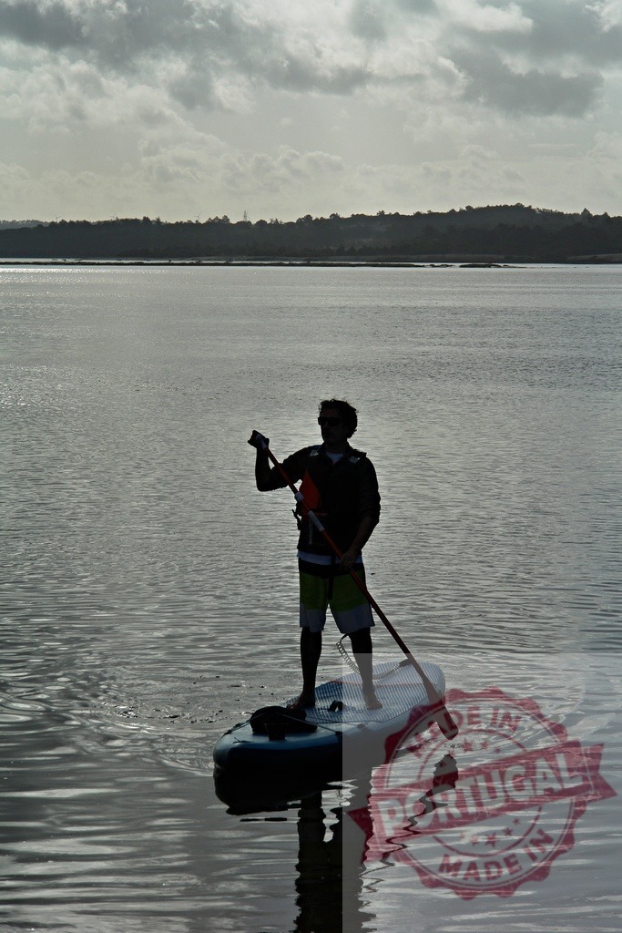 Man paddleboarding enjoying quiet water sport activity | Man paddleboarding on calm water, silhouette against cloudy sky - Realized with Pictrs.com