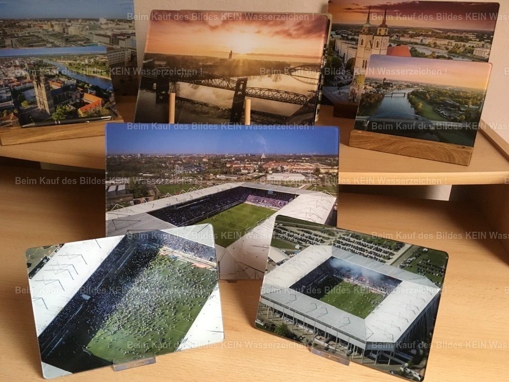 luftbild-magdeburg-tisch-magdeburger-platte-steffen-lehmann_0863 | Auf diesem Foto sind verschiedene „Magdeburger Platten®“ mit Motiven rund um den 1. FC Magdeburg zu sehen – darunter das Stadion und Bilder aus einer besonderen Zeit: dem Aufstieg in die 2. Fußball-Bundesliga.Für mich war das eine schöne Möglichkeit, nicht nur ein bekanntes Magdeburger Motiv auf Acrylglas zu bringen, sondern auch einen besonderen Moment der Stadt und ihrer Fußballgeschichte festzuhalten. Die „Magdeburger Platte®“ konnte damit ganz unterschiedliche Seiten Magdeburgs zeigen – von Stadtansichten aus der Luft bis hin zu Motiven, mit denen viele Menschen ganz persönliche Erinnerungen verbinden. - Realisiert mit Pictrs.com