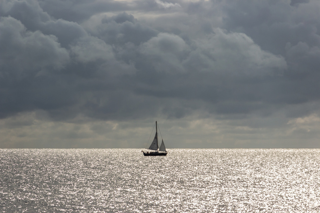 Wandbild: Segelboot vor dunklen Wolken in Damp | Dieses Wandbild im Querformat zeigt ein Segelboot auf der Ostsee bei Sonnenschein und dunklen Wolken.  - Realisiert mit Pictrs.com