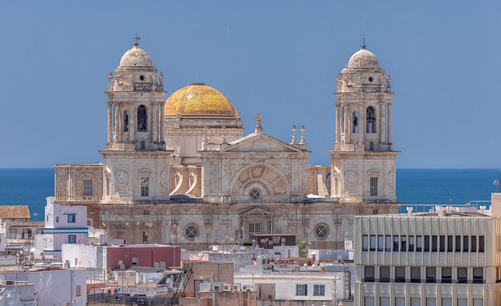 Die Kathedrale von Cádiz in Andalusien, Meer als Hintergrund | Das Bild zeigt die Kathedrale von Cádiz, offiziell bekannt als "Catedral de Santa Cruz". Details zur Kathedrale:Standort: Die Kathedrale befindet sich in der spanischen Stadt Cádiz in Andalusien.Architektur: Sie ist bekannt für ihre markante goldene Kuppel und die beiden Türme. Sie wurde unter anderem mit Austernstein gebaut. - Realisiert mit Pictrs.com