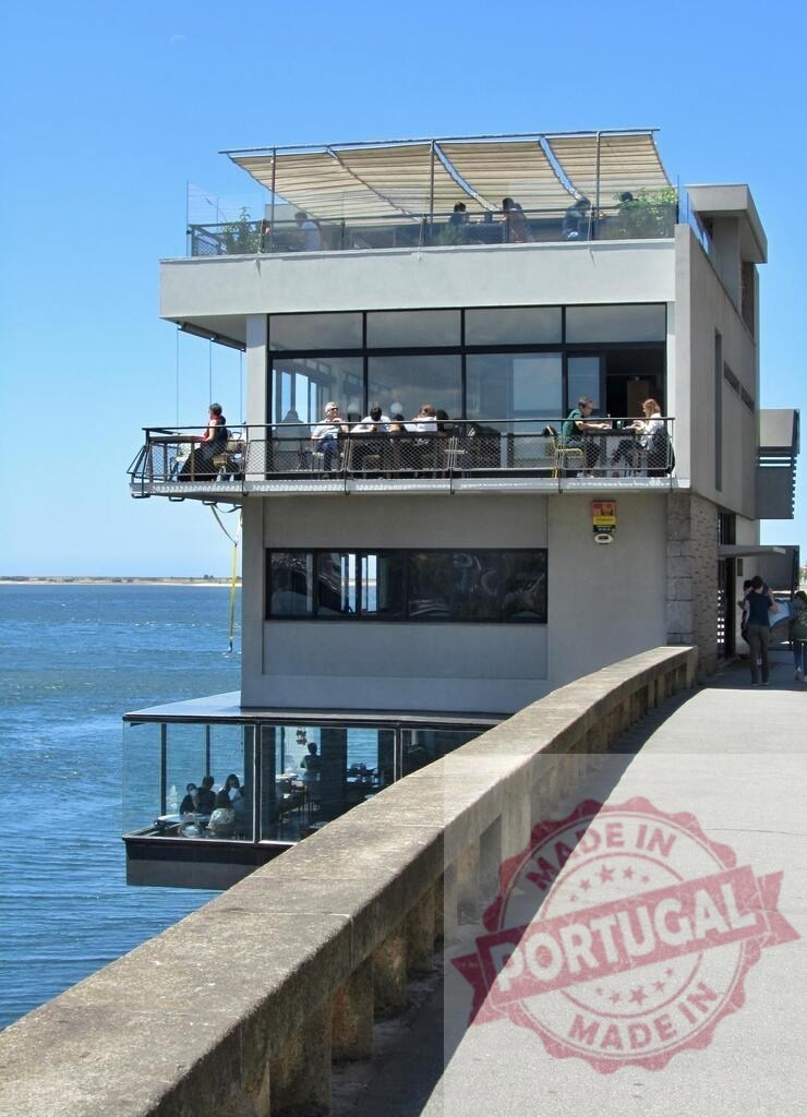 Modern riverfront restaurant building with outdoor dining in Foz do Douro | People enjoying food and drinks at a restaurant on the Douro River on a sunny day - Realized with Pictrs.com