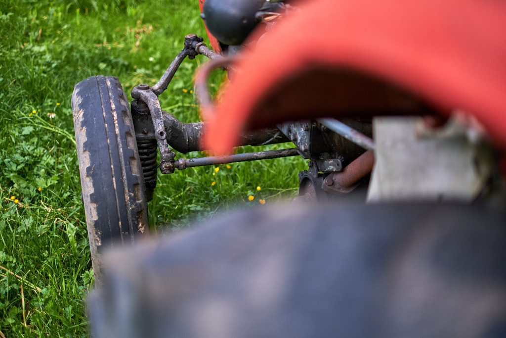 Vorderrad eines alten roten Traktors | Bizau, Austria - July 07, 2021: Vorderrad eines alten roten Traktors der in der Wiese steht. - Realisiert mit Pictrs.com
