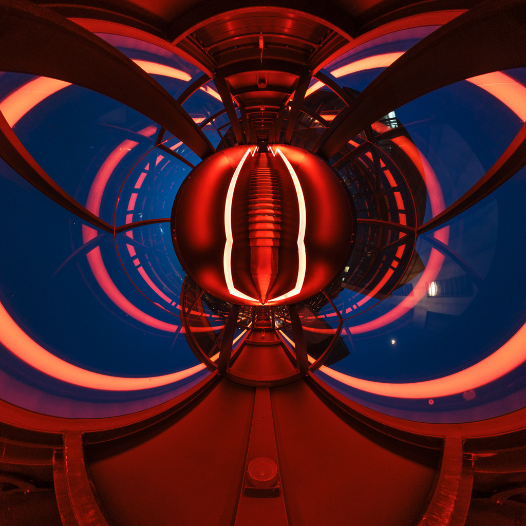 Wandbild: Abstrakte futuristische Perspektive | Dieses faszinierende Wandbild zeigt eine hypermoderne Innenansicht mit einem einzigartigen, nahezu außerirdischen Design. Die Szene wird von kräftigen roten und blauen Lichtern dominiert, die durch die Wölbung der Architektur verzerrt und reflektiert werden. In der Mitte des Bildes sticht ein symmetrisches, rot beleuchtetes Element hervor, das die Aufmerksamkeit des Betrachters sofort auf sich zieht. Die geometrischen Muster und die intensiven Farben erzeugen eine dynamische und hypnotische Atmosphäre, die an eine Szene aus einem Science-Fiction-Film erinnert. Dieses Bild verleiht jedem Raum eine moderne und futuristische Note und lädt den Betrachter ein, sich in einer anderen Welt zu verlieren.