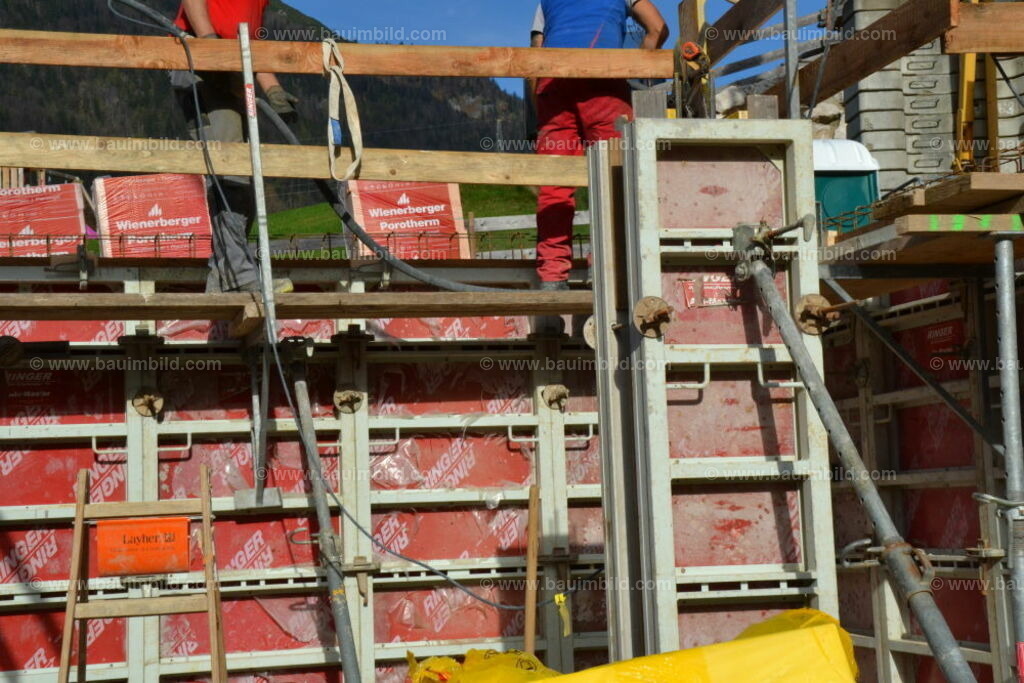 Wandschalung mit Schutzgerüst | Auf Schutzgerüst stehende Arbeiter mit Betonrüttler bereit zum Betonieren einer geschalten und bewehrten Betonwand