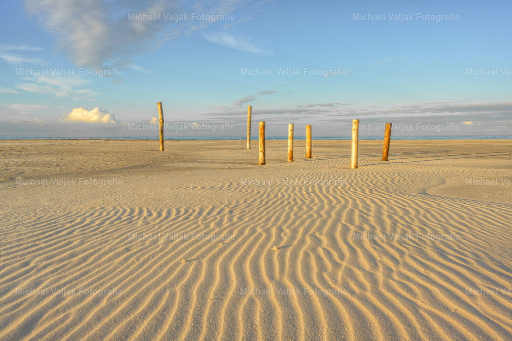 Holzpfähle auf dem Kniepsand auf Amrum | Der Kniepsand auf Amrum ist eine faszinierende geologische Erscheinung. Obwohl er scheinbar ein Teil der Insel ist, gehört er geologisch gesehen nicht zu Amrum und ist eine eigenständige Sandbank. Diese bietet nicht nur Schutz für die Insel gegen Sturmfluten, sondern ist auch ein beliebtes Ziel für ausgedehnte Strandwanderungen und Naturbeobachtungen. Die Pfähle im Sand sind Zeugen menschlicher Aktivitäten und dienen oft als Orientierungspunkte für Besucher auf ihren Entdeckungstouren entlang dieses einzigartigen Naturwunders. - Realisiert mit Pictrs.com