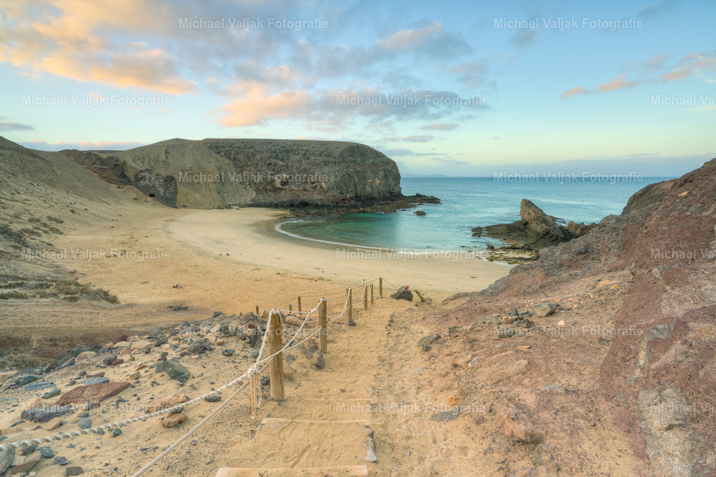 Playa de Papagayo auf Lanzarote | Der Playa de Papagayo im Süden Lanzarotes gehört zu den eindrucksvollsten Stränden der Insel. Die geschützte Bucht liegt im Naturgebiet Los Ajaches und besticht durch goldenen Sand, ruhiges türkisfarbenes Wasser und dunkle vulkanische Felswände, die wie ein natürlicher Halbkreis wirken.Wer die kurze Schotterpiste auf sich nimmt, wird mit einer der klarsten und atmosphärischsten Küstenlandschaften der Insel belohnt – ideal zum Schwimmen, Schnorcheln und Fotografieren. - Realisiert mit Pictrs.com