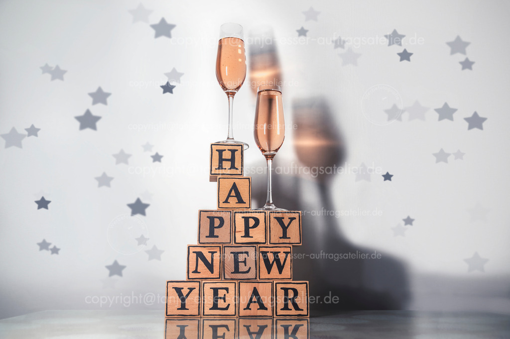 Glasses with Rosy champagne make a colored shadow and wooden cubes form the text happy new year | Gläser mit Rosy Champagner machen einen farbigen Schatten und Holzwürfel bilden den Text happy new year. Sylvester. 