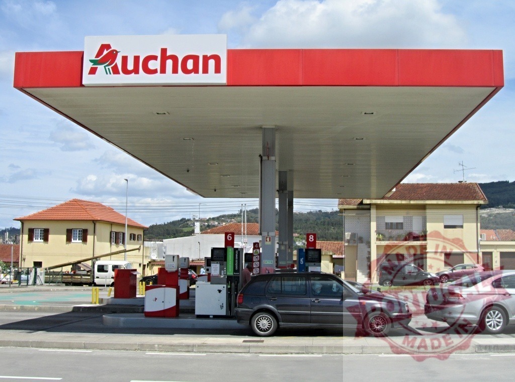 Auchan gas station with cars refueling at pumps | Auchan gas station with multiple cars refueling under a red canopy on a sunny day - Realized with Pictrs.com