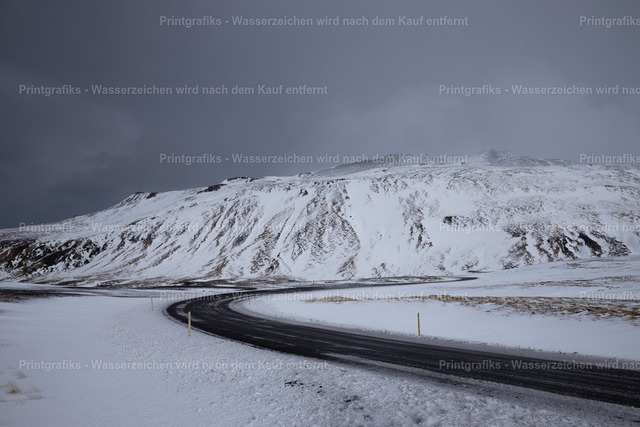 Straße durch die Winterlandschaft Islands | Eine dunkle Straße führt durch eine weite, schneebedeckte Landschaft in Island. Die kargen Berge, der schwere Himmel und der starke Kontrast zwischen Asphalt und Schnee erzeugen eine stille, raue und einsame Winterstimmung. - Realisiert mit Pictrs.com