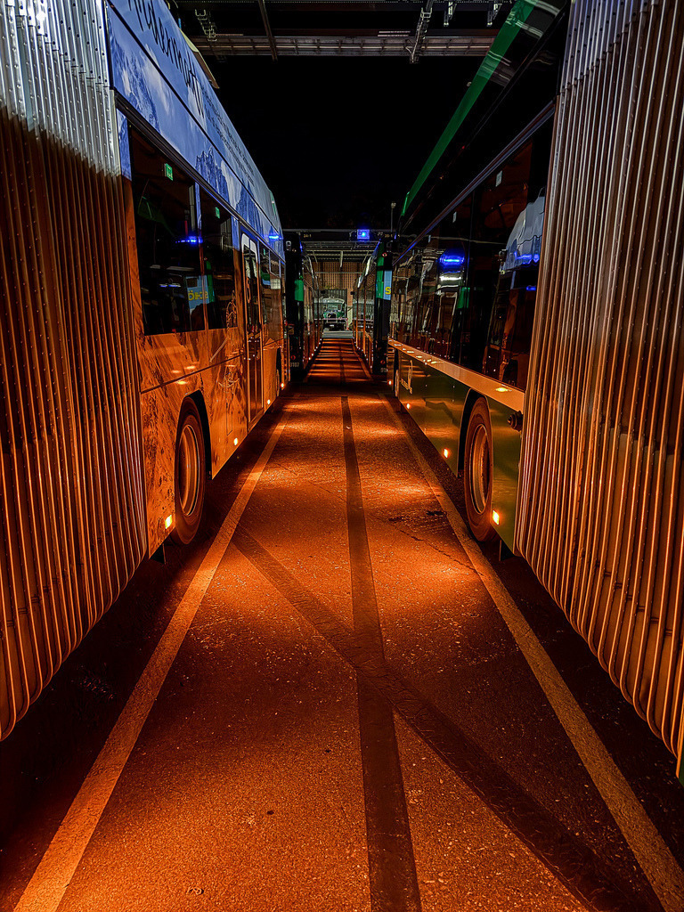 Nachtschicht – Urbane Industrial-Fotokunst Gelenkbusse | Eine atmosphärische, tiefgründige Momentaufnahme der urbanen Nacht. Fotografiert um 3:37 Uhr morgens, fängt diese Fine-Art-Aufnahme ruhende Gelenkbusse in einem spektakulären Zusammenspiel aus harten Schatten, metallischen Texturen und intensivem Kunstlicht ein. Die kraftvolle Fluchtlinien-Perspektive bringt eine moderne, raue Industrial-Atmosphäre in jeden Raum. Ein absolutes Highlight für modernes Interior Design und urbane Lofts. Empfohlen auf gebürstetem Alu-Dibond für eine einzigartige Metall-Optik. - Realisiert mit Pictrs.com