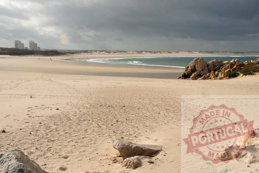 Peniche beach with dark stormy clouds over ocean. Centro - Portugal | Peniche beach featuring sand, rocks, and ocean waves under a dramatic cloudy sky in Portugal - Realized with Pictrs.com