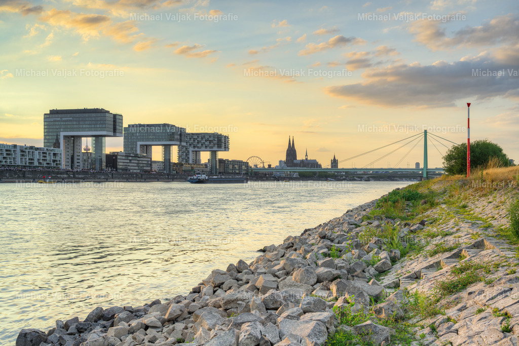 Am Rheinufer bei den Poller Wiesen in Köln | Bei Niedrigwasser zeigt sich das steinige Rheinufer bei den Poller Wiesen von seiner charakteristischen Seite. Die tief stehende Sonne taucht die Ufersteine und den Rhein in warmes, goldenes Abendlicht und schafft eine besondere Atmosphäre zwischen Tag und Nacht.Der Blick direkt vom Rheinufer über den Fluss verbindet die natürliche, ursprüngliche Landschaft des Rheins mit der Kölner Stadtkulisse. Das warme Licht des Sonnenuntergangs und die markanten Strukturen des steinigen Ufers verleihen dem Motiv eine authentische und stimmungsvolle Wirkung.Ein atmosphärisches Landschaftsfoto von Köln am Rhein, das die besondere Schönheit des Flusses bei Niedrigwasser und im Licht der untergehenden Sonne einfängt. - Realisiert mit Pictrs.com