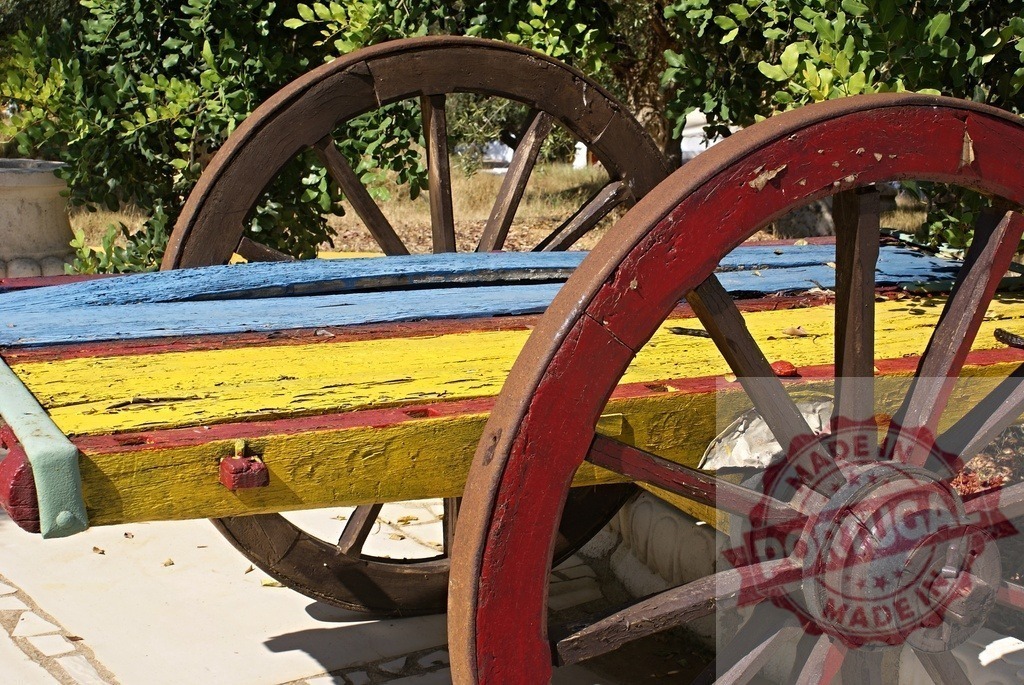 Vintage wooden cart with primary colors in a garden | Weathered wooden cart showing red, yellow, and blue paint against green foliage - Realized with Pictrs.com