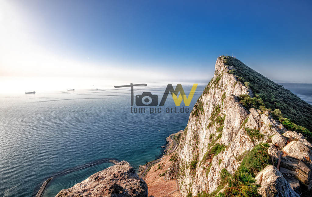 Der Monolith-----Felsen von Gibraltar----Rock of Gibraltar | Das Bild zeigt den Felsen von Gibraltar (Rock of Gibraltar). Dieser monolithische Kalksteinfelsen ist ein britisches Überseegebiet an der Südspitze Europas und trennt das Mittelmeer vom Atlantik. Hier sind einige Details:Der Felsen ist ein markantes Wahrzeichen, das größtenteils aus Kalkstein besteht und eine Höhe von 426 Metern erreicht. Er ist bekannt für seine strategische militärische Lage und ein wichtiges Naturschutzgebiet, das die einzigen wilden Affen Europas, die Berberaffen, beheimatet.  - Realisiert mit Pictrs.com