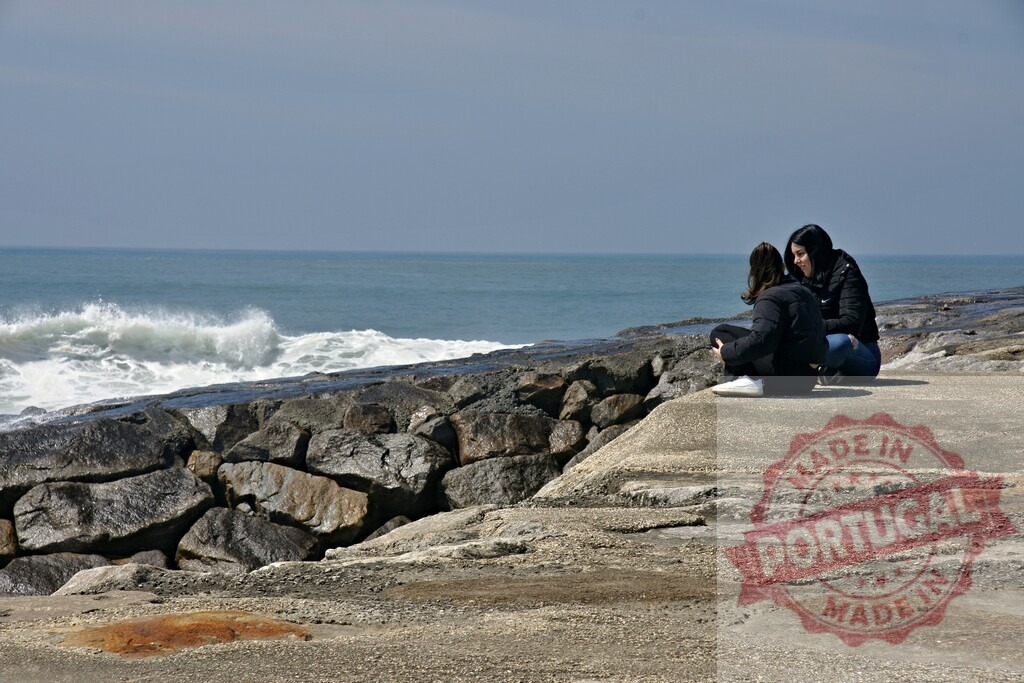 Aveiro Region - Portugal Two women bonding talking by ocean waves | Two women sitting on rocks conversing near the ocean, enjoying the outdoors together - Realized with Pictrs.com