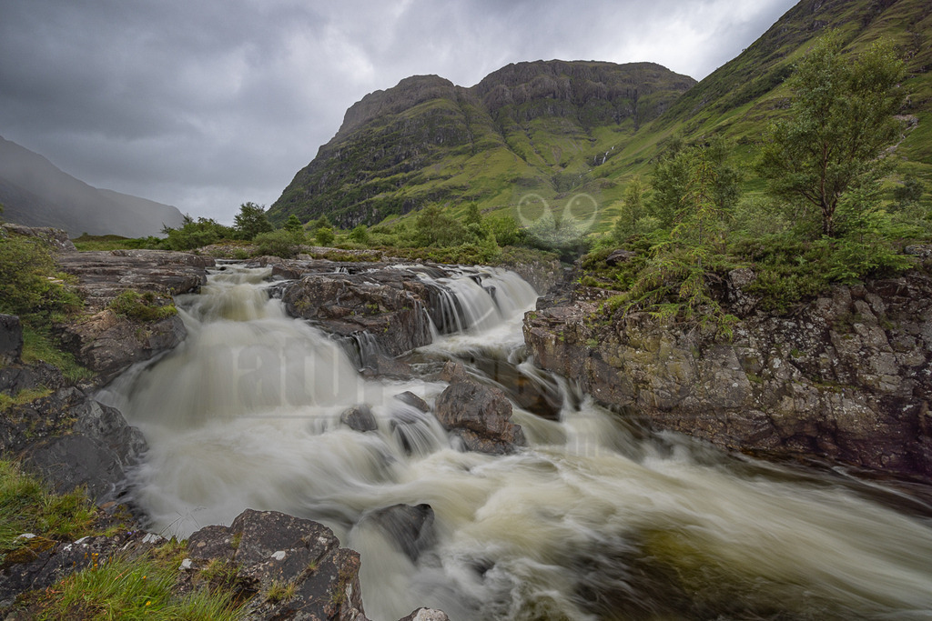 20220725130332-5 | Diese atemberaubende Aufnahme fängt die wilde Schönheit der schottischen Highlands ein. Ein reißender Fluss stürzt über schroffe Felsen und formt eine Reihe von kleinen Wasserfällen, deren tosendes Rauschen man fast hören kann. Die steilen, mit Gras bewachsenen Berge im Hintergrund bilden einen imposanten Rahmen für dieses Naturschauspiel. Der Himmel ist bedeckt, was der Szene eine dramatische und melancholische Atmosphäre verleiht. Die üppige Vegetation am Flussufer zeugt von der Feuchtigkeit und dem gemäßigten Klima dieser Region. Es ist ein typisches Bild der schottischen Highlands, das die rohe und ungezähmte Schönheit dieser Landschaft widerspiegelt. - Realisiert mit Pictrs.com