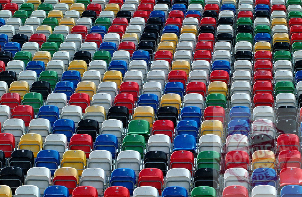 Colorful stadium seats creating a vibrant pattern for sporting event | Rows of empty multicolored plastic chairs forming a repeating pattern in a stadium, ready for fans - Realized with Pictrs.com