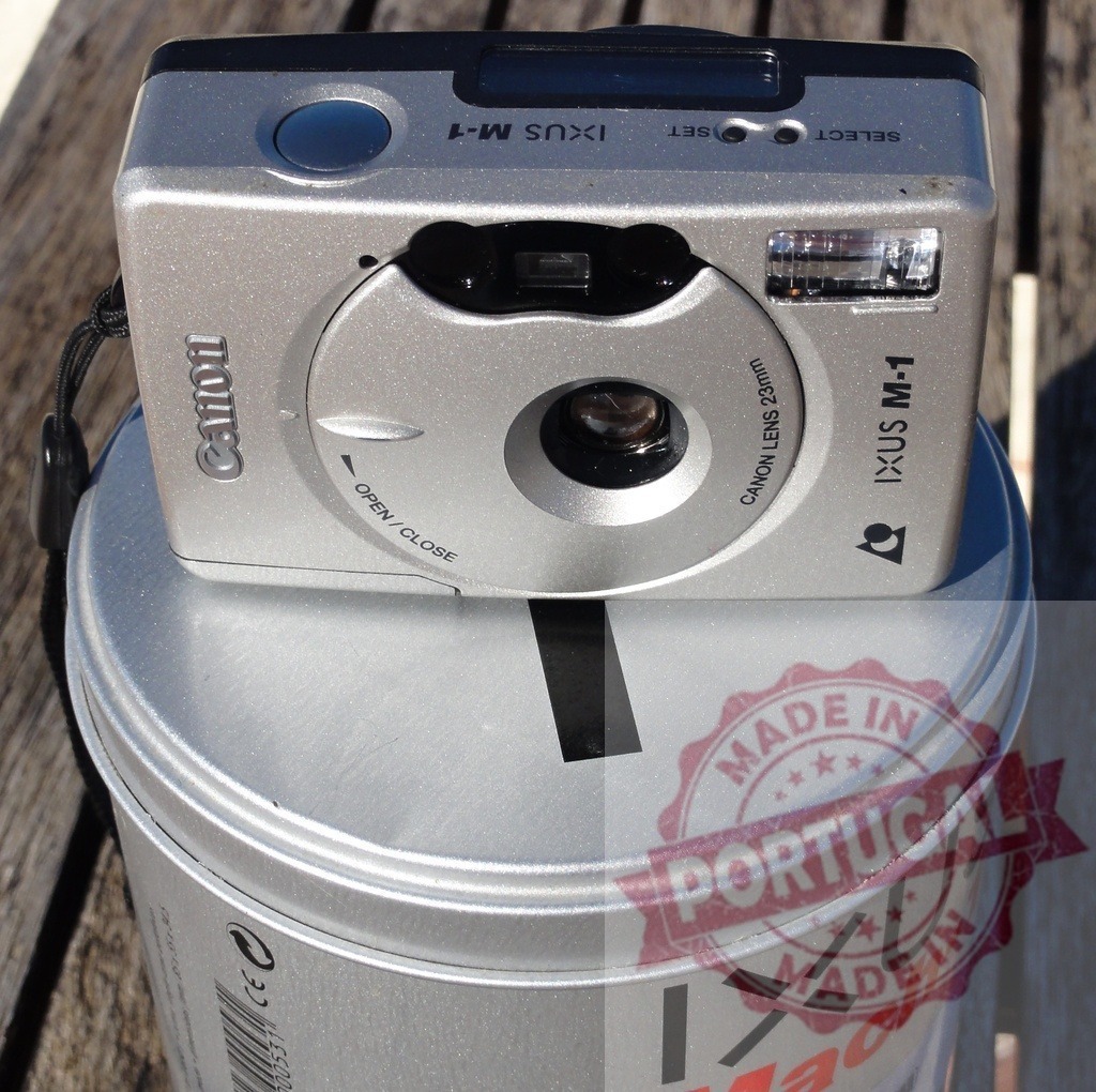 Canon IXUS M-1 camera on metal tin | Vintage Canon IXUS M-1 film camera resting on a cylindrical metal tin - Realisiert mit Pictrs.com