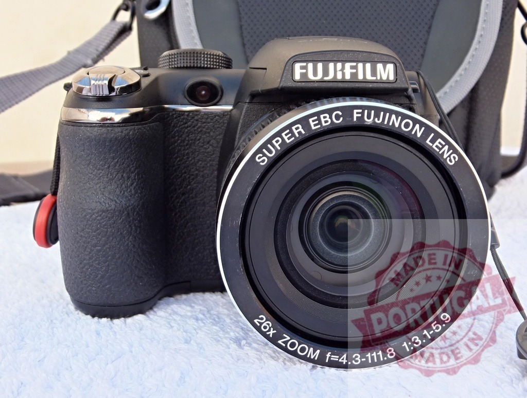 Fujifilm digital camera with Super EBC Fujinon lens | Fujifilm digital camera black body and Fujinon zoom lens details, with a camera bag in the background - Realisiert mit Pictrs.com