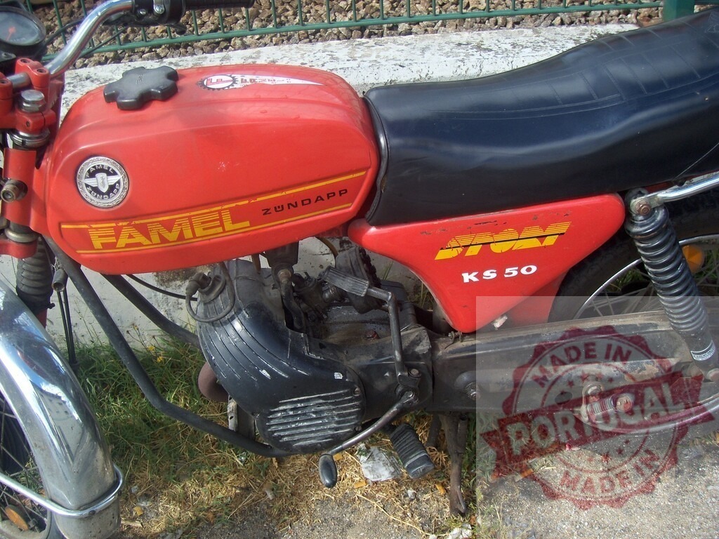 Red Famel Zündapp KS 50 motorcycle parked near a low wall | Close-up of a vintage red Famel Zündapp KS 50 motorcycle parked outdoors near a low wall - Realized with Pictrs.com