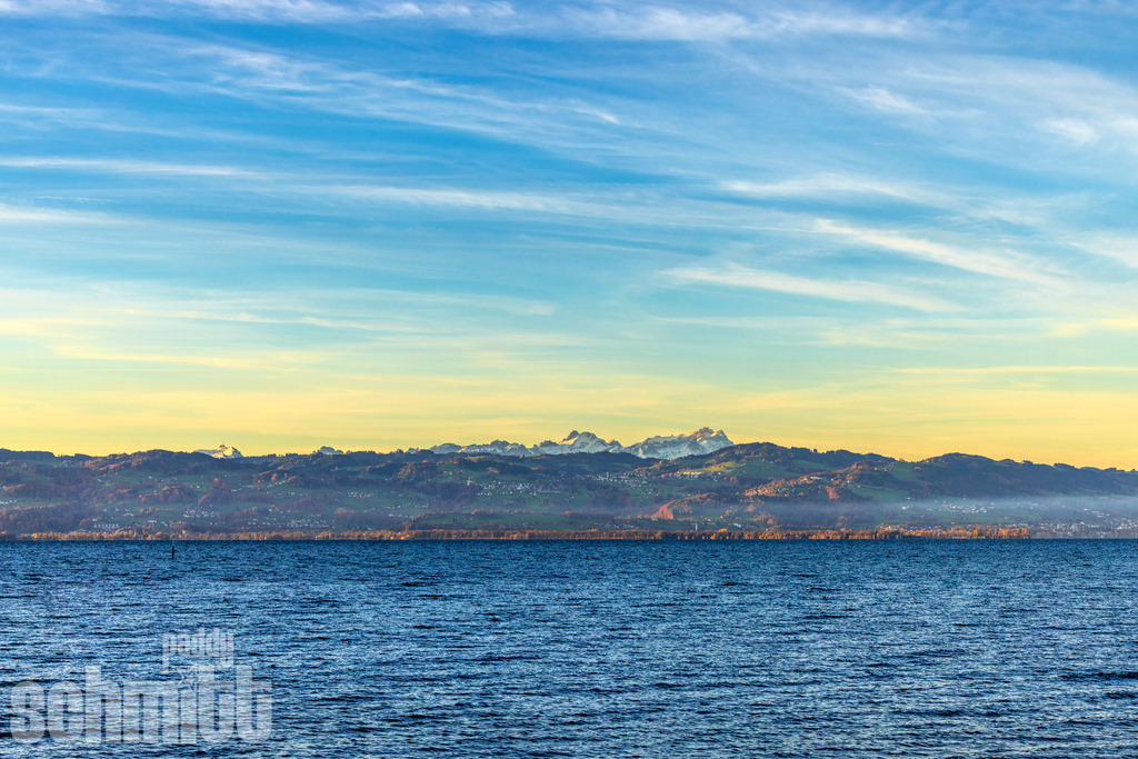 Bergpanorama am Bodensee im Frühling | m Frühling zeigt sich der Bodensee vor einer beeindruckenden schneebedeckten Bergkulisse von seiner besonders farbenfrohen Seite. Frisches Grün, klare Bergsilhouetten und das ruhige Wasser verbinden sich zu einer harmonischen Landschaftsaufnahme voller Leichtigkeit und Weite. - Realisiert mit Pictrs.com