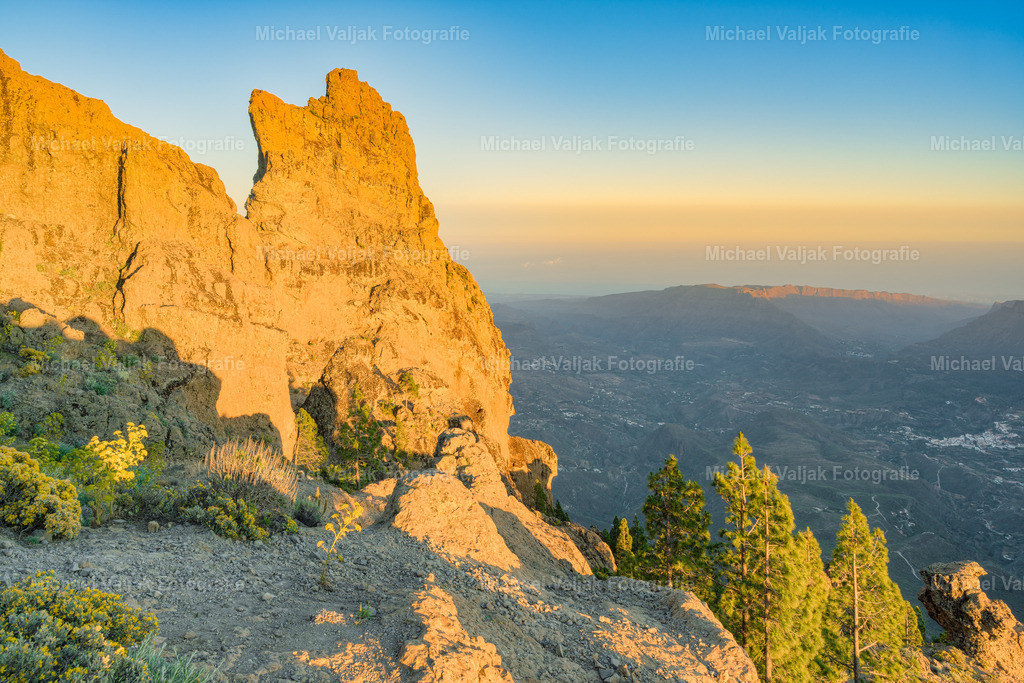 Morro de la Agujereada auf Gran Canaria | Die Abendsonne taucht den Morro de la Agujereada in ein warmes, goldenes Licht und offenbart die raue Schönheit dieses höchsten Gipfels Gran Canarias. Mit seinen 1.956 Metern thront er majestätisch über der Insel und wirkt in der Dämmerung beinahe mystisch – ein Ort, an dem die Natur ihre ganze Erhabenheit entfaltet.Wenn die letzten Sonnenstrahlen auf die zerklüfteten Felsen treffen, entstehen dramatische Kontraste zwischen Licht und Schatten, die die einzigartige Struktur des Berges noch betonen. - Realisiert mit Pictrs.com