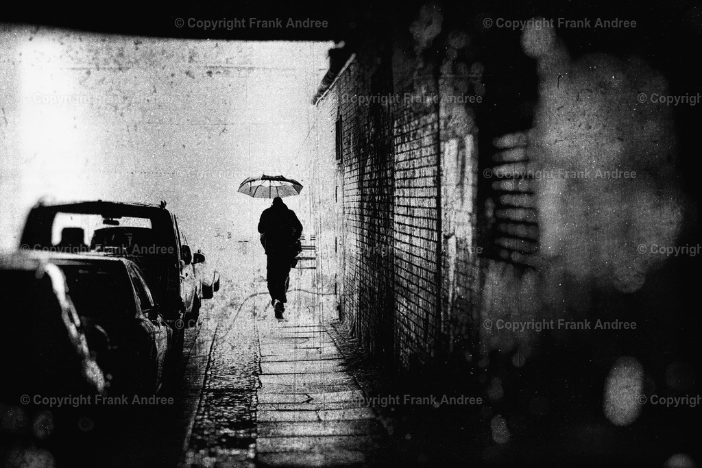 Regen in Berlin | Ein Mann mit Regenschirm am Ende eines Tunnels in Berlin an einem regnerischen Tag. Abstrakte Straßenfotografie aus Berlin in schwarz weiß. - Realisiert mit Pictrs.com