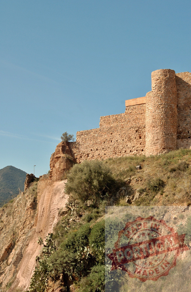 Ancient castle ruins standing on a rocky hill | Castle ruins with stone walls and a circular tower on a steep arid hillside under a clear sky - Realized with Pictrs.com