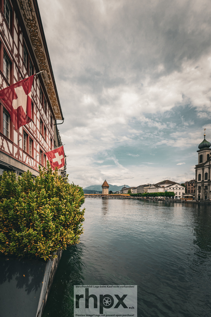 Luzerner Reussufer mit Wasserturm | Heimat. Wasser. Weite.Der Blick entlang des Reussufers vereint die ikonischen Wahrzeichen Luzerns in einer harmonischen Komposition. Die wehenden Schweizer Fahnen und das ruhige Wasser schaffen eine Atmosphäre von Beständigkeit und zeitloser Eleganz.Wähle unter "Produktauswahl" dein Wunschformat: Vom klassischen Wandbild über Puzzle &amp; Tassen bis zum digitalen Download (z.B. als Handy-Hintergrund). - Realisiert mit Pictrs.com