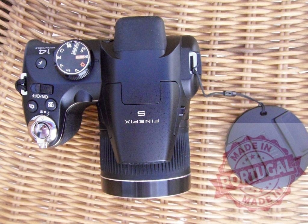 Fujifilm FinePix digital bridge camera on wicker surface | Fujifilm FinePix S digital bridge camera with lens cap resting on a wicker background - Realisiert mit Pictrs.com